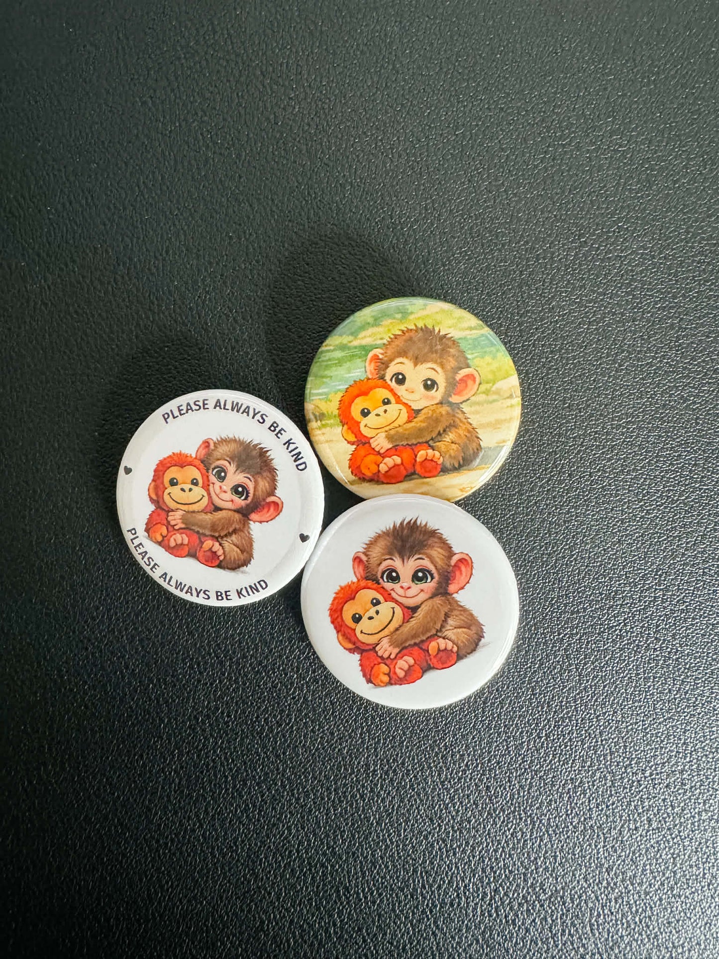 Three circular pins with monkey illustrations on a dark surface