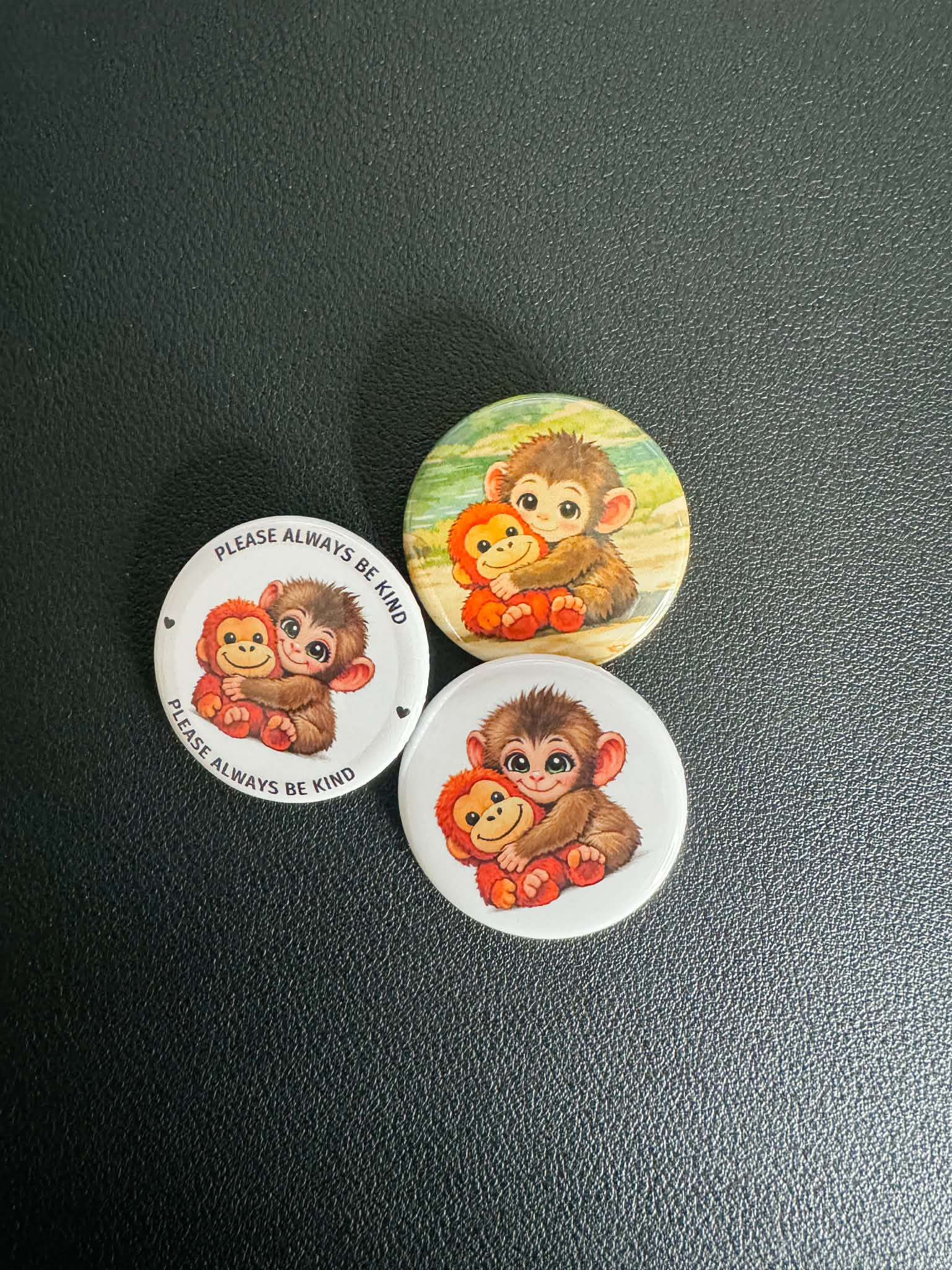 Three circular pins with monkey illustrations on a dark surface
