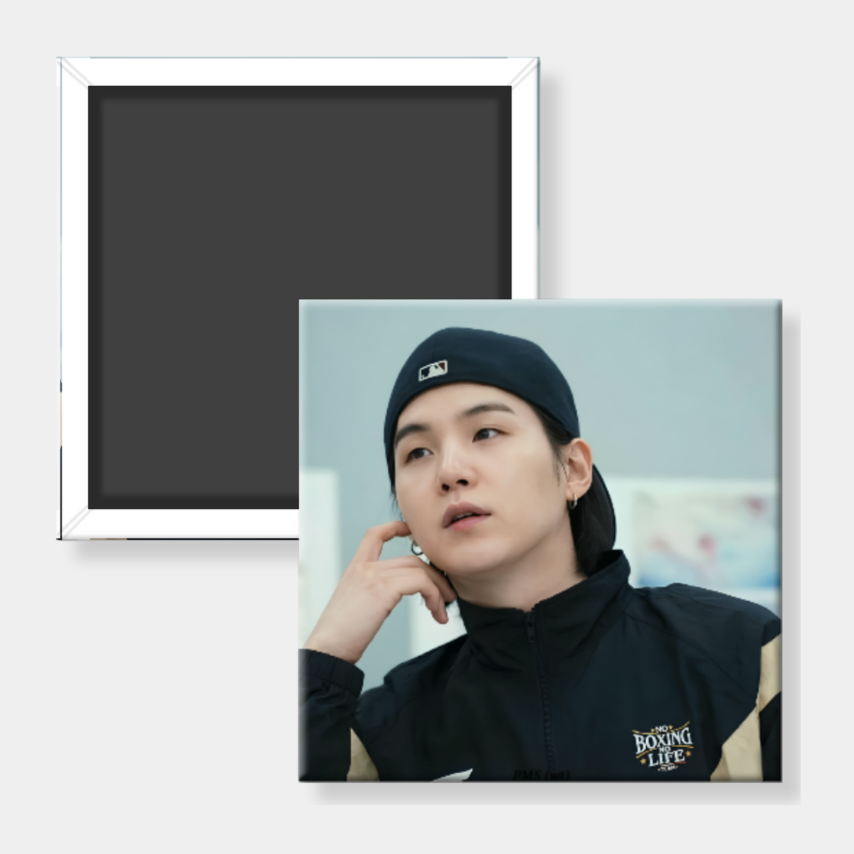 A square custom photo magnet showing a portrait of a man in a black cap and jacket, displayed alongside its plain black magnetic back with a silver metal frame on a light gray background.