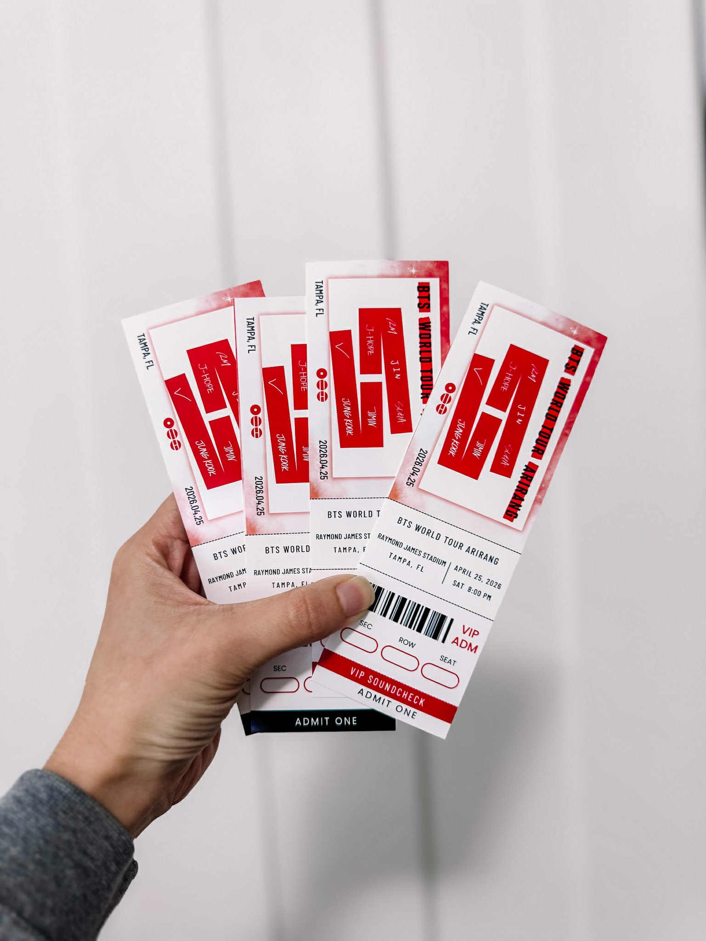 Hand holding multiple concert tickets against a plain background